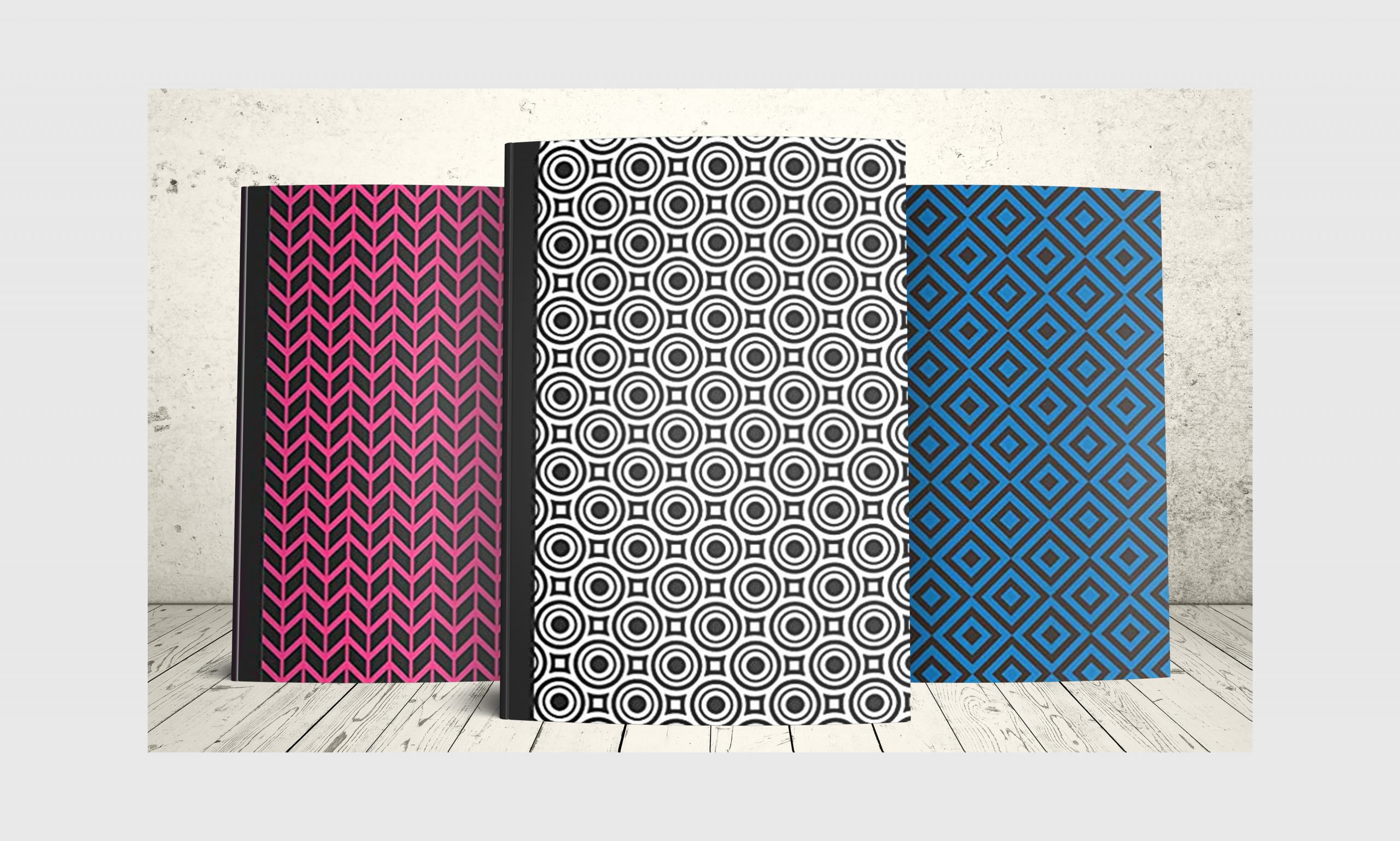 Three journal notebooks with geometric designs on the cover in pink and black, blue and black and white and black.